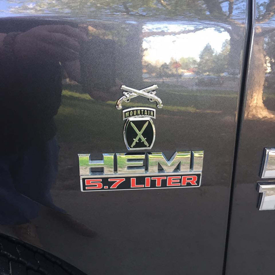 A close-up of a black vehicle door featuring a chrome and red 'FORD TATTOO HEMI 5.7 LITER' badge, with reflections of a person and outdoor scenery on the glossy paint.