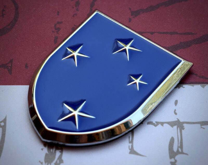 A shield-shaped metallic badge with a blue enamel center, four silver stars, and a polished chrome border, shown on a split red and white background.