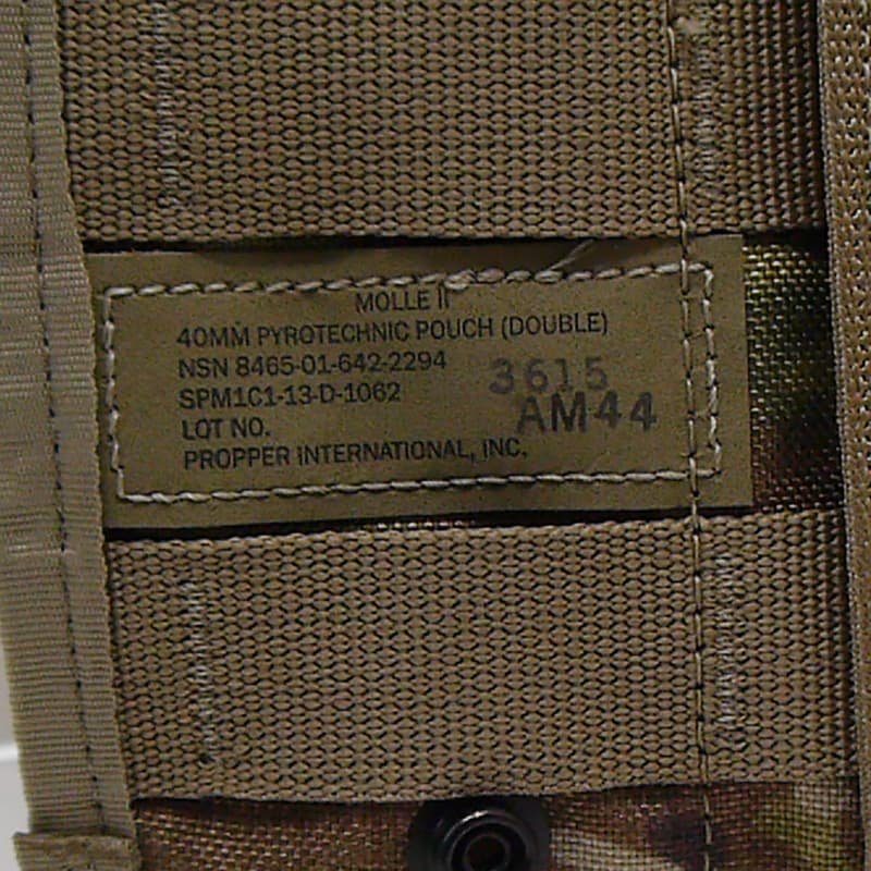 Close-up of a tan nylon MOLLE webbing panel with a sewn-in label reading 'MOLLE II 40MM PYROTECHNIC POUCH (DOUBLE)' and 'PROPER INTERNATIONAL, INC.', plus stamped numbers.