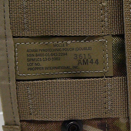 Close-up of a tan nylon MOLLE webbing panel with a sewn-in label reading 'MOLLE II 40MM PYROTECHNIC POUCH (DOUBLE)' and 'PROPER INTERNATIONAL, INC.', plus stamped numbers.