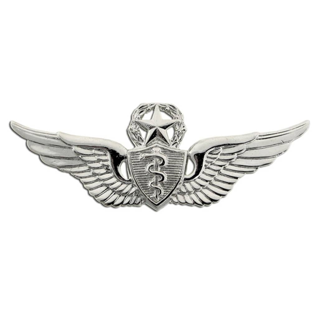 A silver-colored metal military insignia featuring wings, a star, a shield with a caduceus symbol, and a wreath on a plain white background.