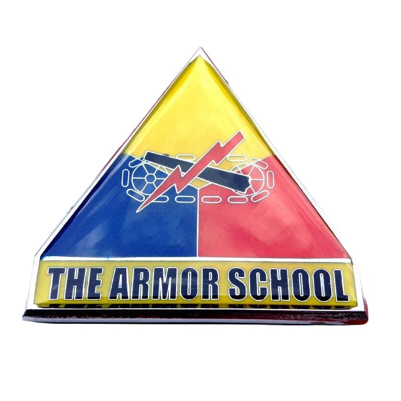 A triangular enamel pin or badge with a yellow top half, blue left half, and red right half, featuring a central emblem and the text 'THE ARMOR SCHOOL' across the bottom. The pin is photographed on a plain white background.