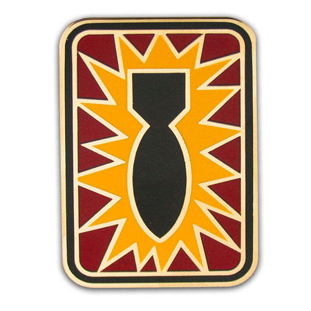 A rectangular enamel pin with rounded corners featuring a black bomb silhouette centered on a yellow starburst background, surrounded by red segments and a gold border, shown on a white background.