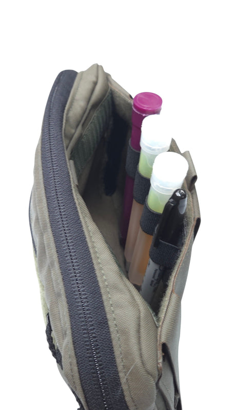 A close-up of a beige tactical pouch with a dark gray zipper, shown open with several pens and lip balm tubes stored inside, set against a plain white background.