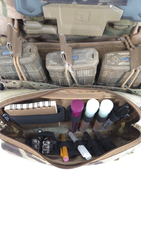 An open tactical utility pouch filled with various small accessories, shown against a background of camouflage gear and pouches.