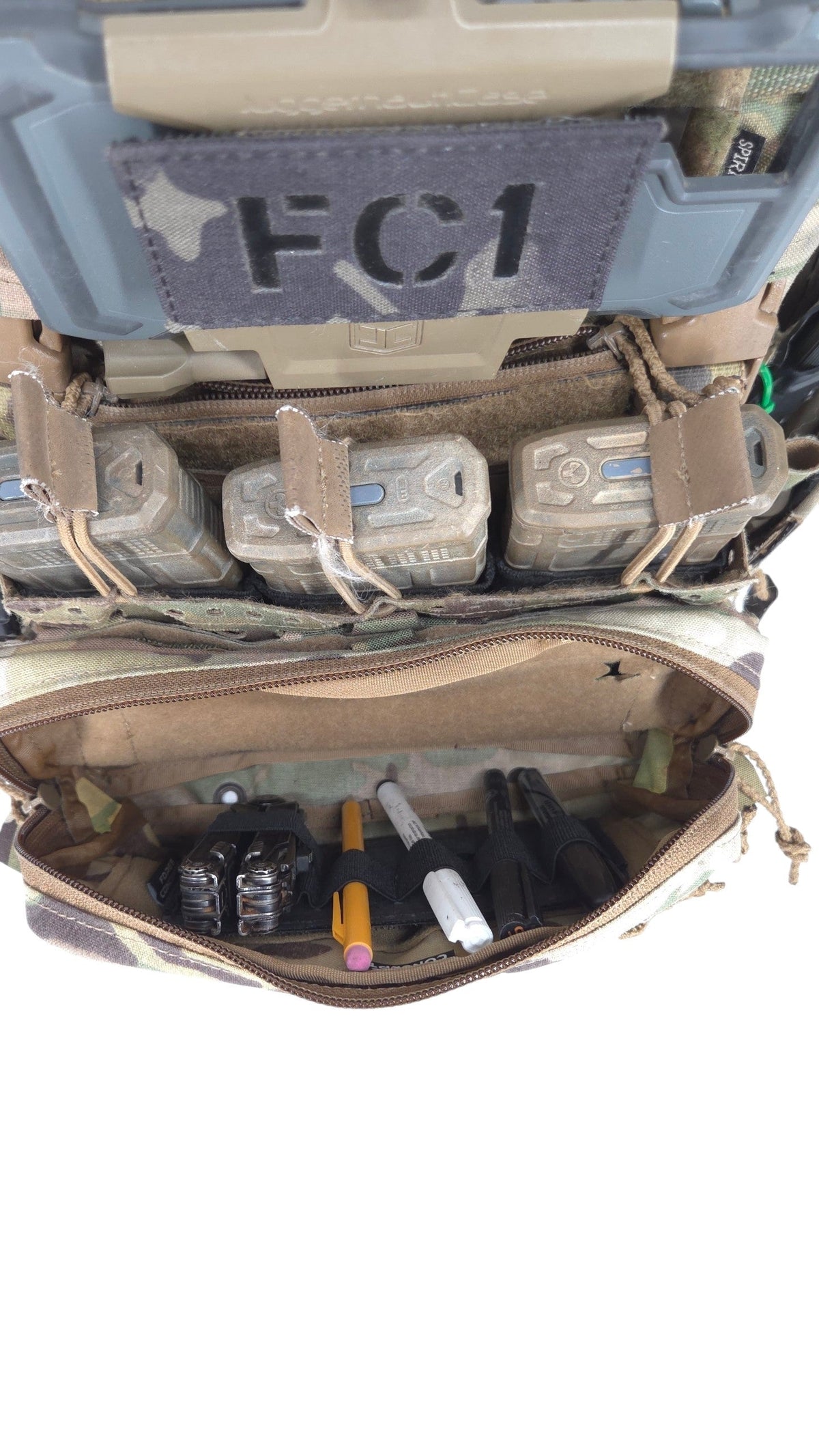 A tactical gear organizer or utility pouch shown open, filled with various small accessories and tools. The pouch has a camouflage pattern exterior and a tan interior, with a dark gray patch on the top that reads 'FC1'.