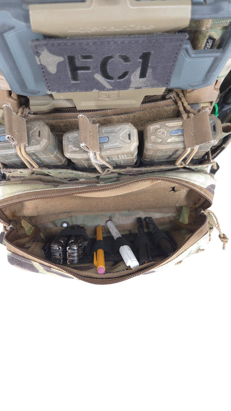 A tactical gear organizer or utility pouch shown open, filled with various small accessories and tools. The pouch has a camouflage pattern exterior and a tan interior, with a dark gray patch on the top that reads 'FC1'.