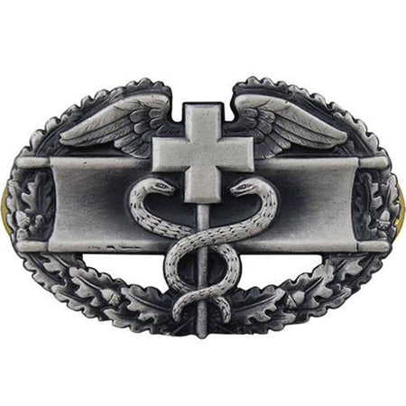 A silver-toned metal belt buckle featuring a medical-themed design with a cross, snake, wings, and laurel wreath on a plain white background.