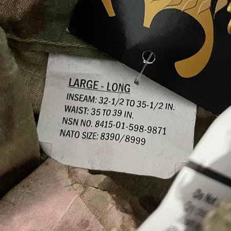 A close-up of a clothing size tag reading 'LARGE - LONG' with measurements for inseam and waist, attached to camouflage fabric near a black and gold garment tag.