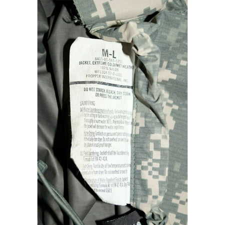 Close-up of a camouflage jacket interior label showing size M-L and care instructions, with gray and green digital camo fabric visible around the collar.