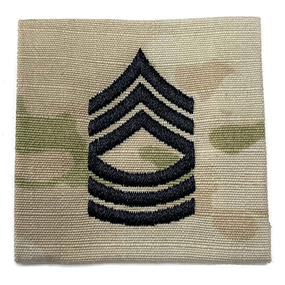 An embroidered military rank insignia patch featuring a black chevron rank symbol on a tan and green camouflage fabric background.