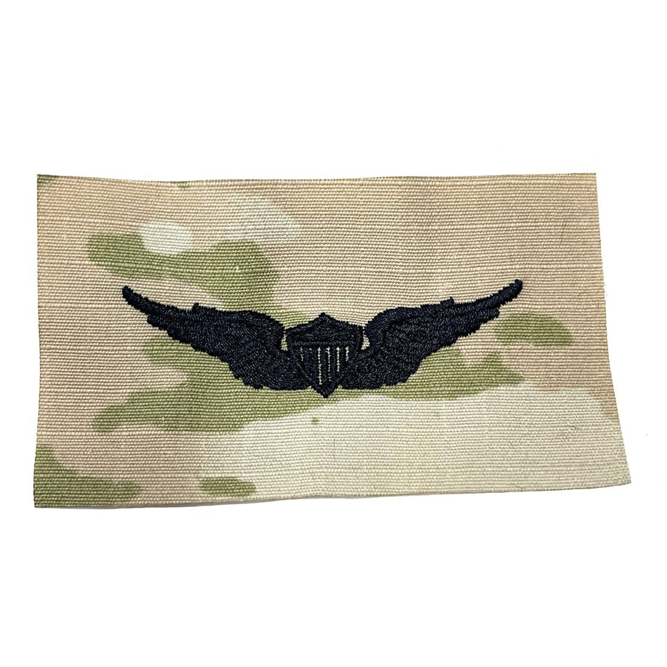 Army Basic Aviator OCP Sew-On Badge featuring a black wings-and-shield insignia centered on a beige camouflage background with muted green and tan tones.