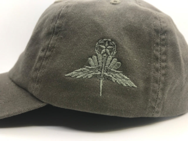 An olive drab green baseball cap featuring an embroidered military-style insignia on the front panel, set against a plain white background.