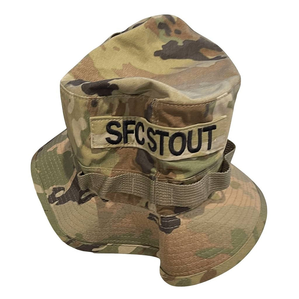 A camouflage boonie hat with a wide brim, featuring a tan patch on the front that reads 'SFC STOUT' in black letters. The hat has a multi-terrain camouflage pattern in shades of green, tan, and brown, and is photographed against a solid white background.