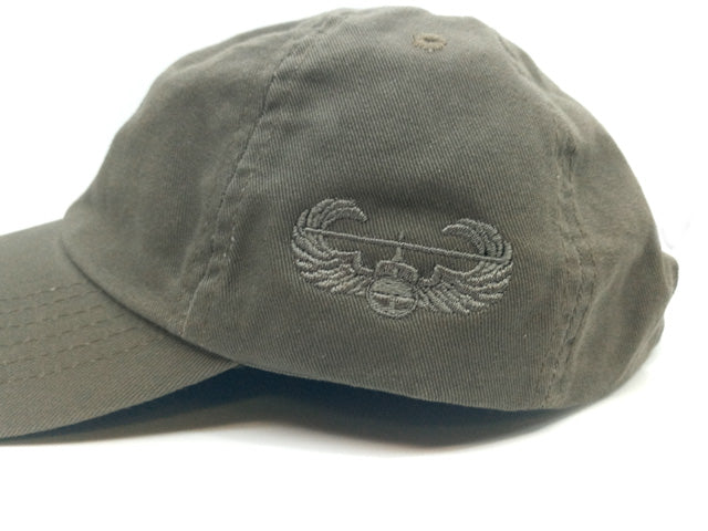 An olive drab baseball cap featuring an embroidered gray Air Force wings emblem on the front, set against a plain white background.