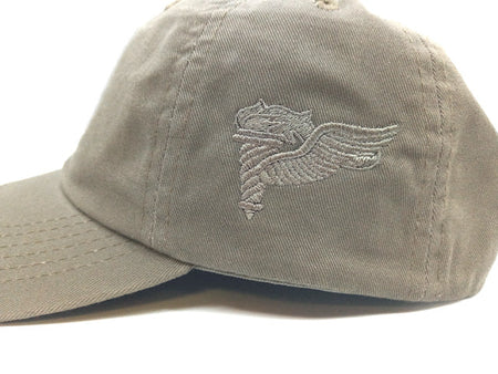 A close-up of a light khaki baseball cap featuring an embroidered gray winged emblem on the front panel, set against a plain white background.