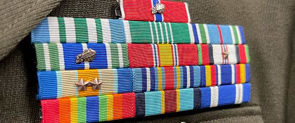 A close-up of military service ribbons and pins displayed on a dark olive green fabric background.
